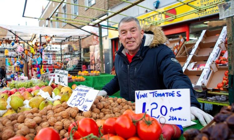 John Papworth Chapel Market trader stood smiling at his stall with vegetables in front of him