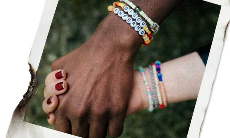 A Black hand holding a white hand with 'disco inferno' bracelets round their wrists