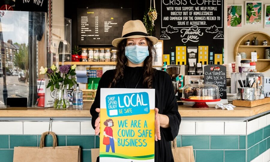 Crisis charity and coffee shop manager pictured with Covid Safe Business poster "Shop Local. We are a Covid Safe business."