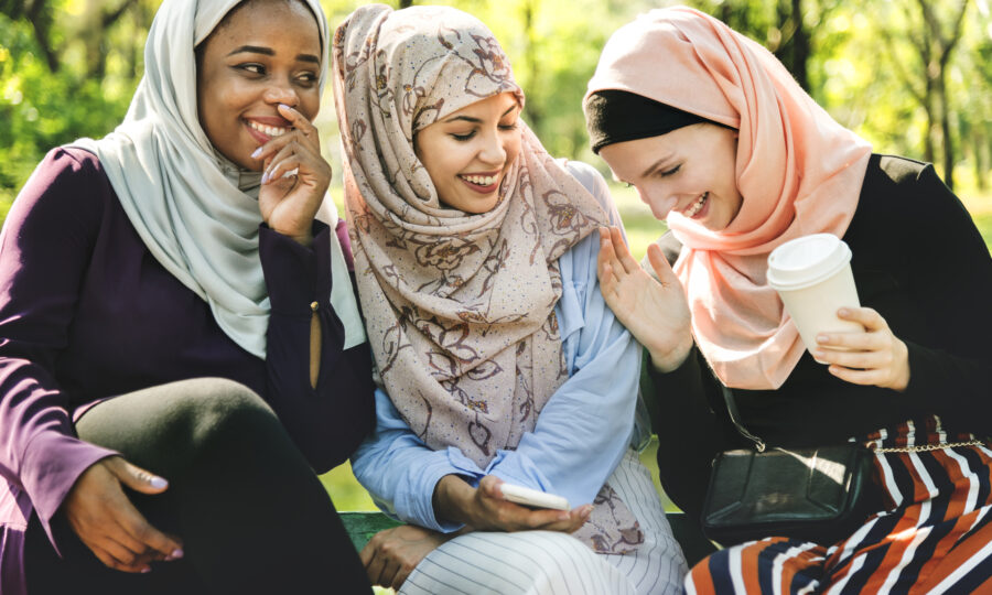 Three women sat together and smiling outdoors