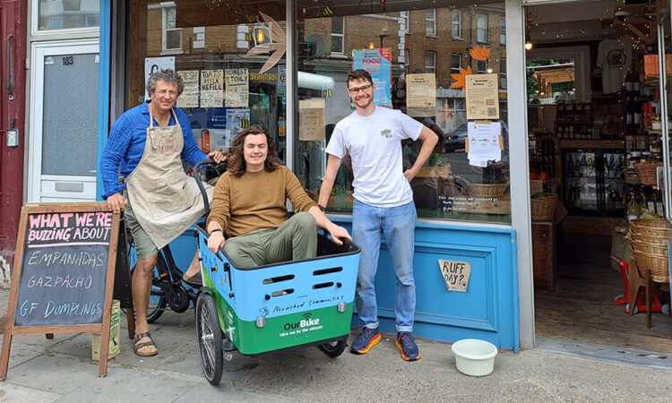 Three members of staff smiling outside Nourished Communities, one of them sat in a cargo bike