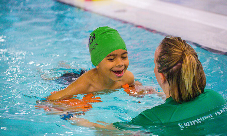 Child in pool with swimming hat on accompanied by adult