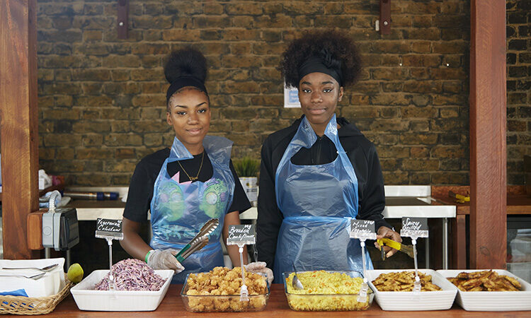 Elyse Duncan-Brown and Santina Robinson stood behind trays of food in Lift youth hub's outdoor kitchen