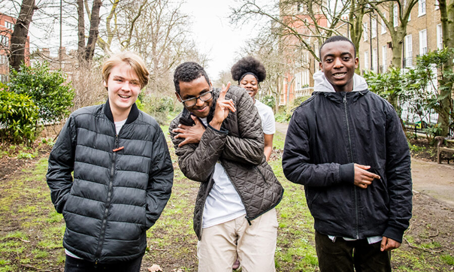 Four youth councillors of different ethnicities smiling, stood outside surrounded by trees