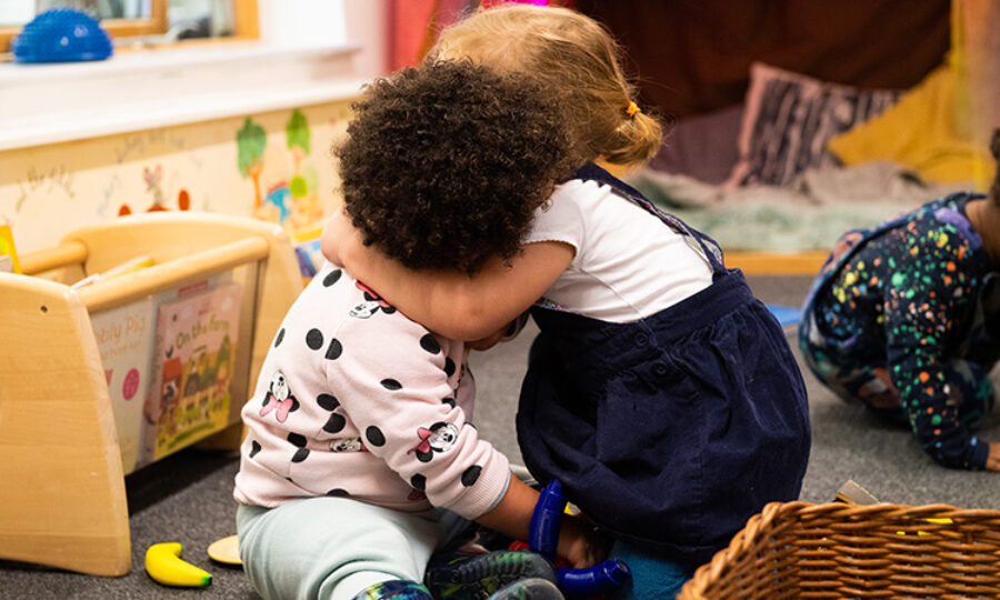 Two young children of mixed ethnicities hugging in a nursery