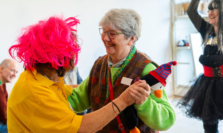 Two people dancing together in fancy dress with a woman in fancy dress dancing with arms in the air in the background