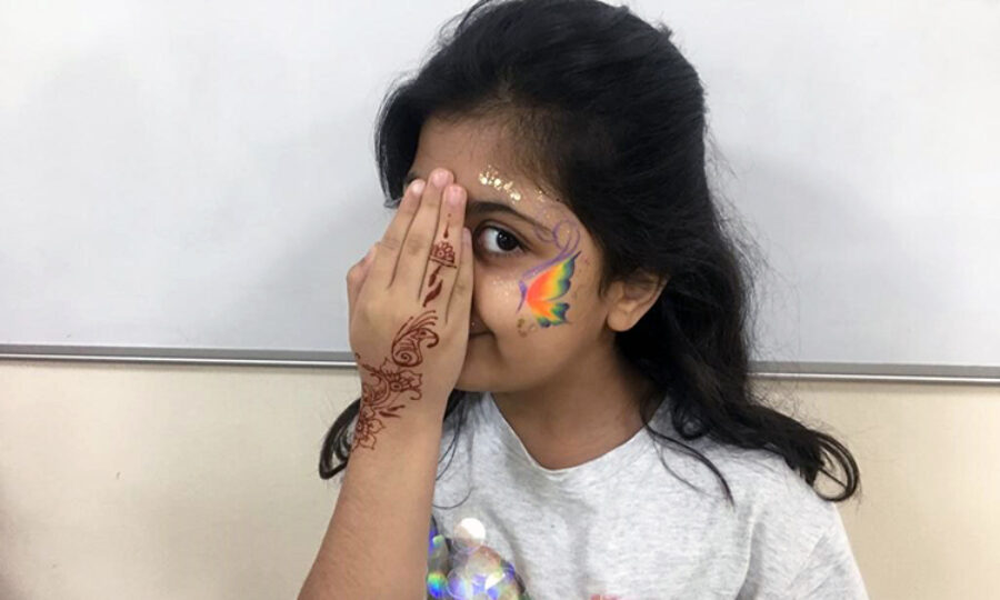 Child with face paint and hand henna holding her hand up to her face