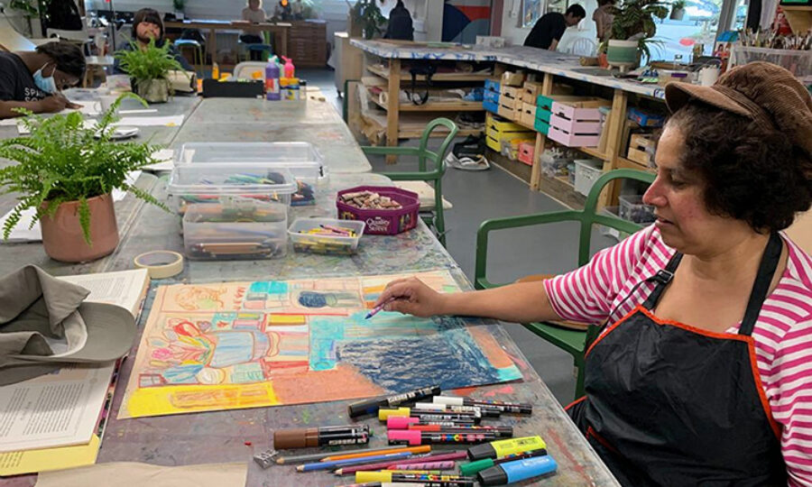 Person sat at a table with art materials and a large, colourful piece of paper