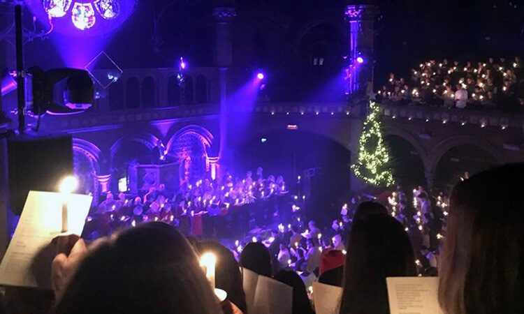 A crowd of people in Union Chapel holding hymn sheets and candles