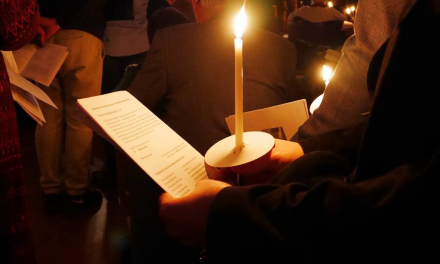Person holding a candle up to a hymn sheet