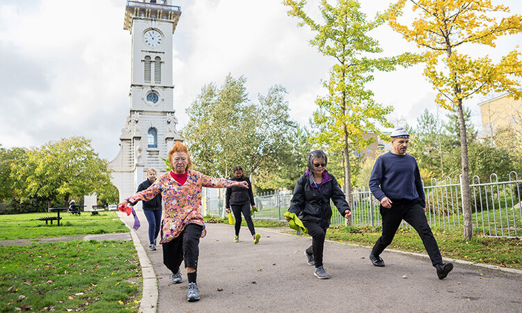 A group of people doing lunges in Caledonian Park, with the Clock Tower in the background