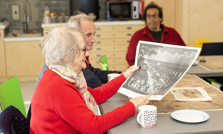 Three older people looking at pictures and having a tea at a table
