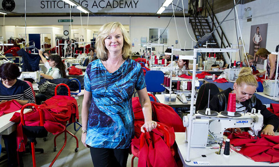 Jenny Holloway stood in a room full of workstations with sewing machines