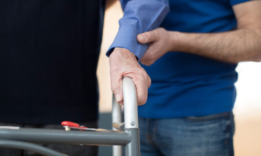 Male social worker helping older person with zimmer frame close up of arms