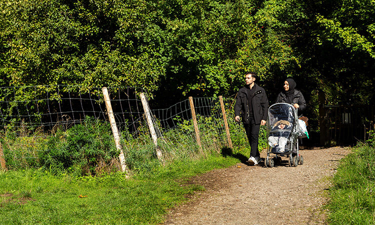 Man walking with a woman in a hijab pushing a pram in Gillespie Park