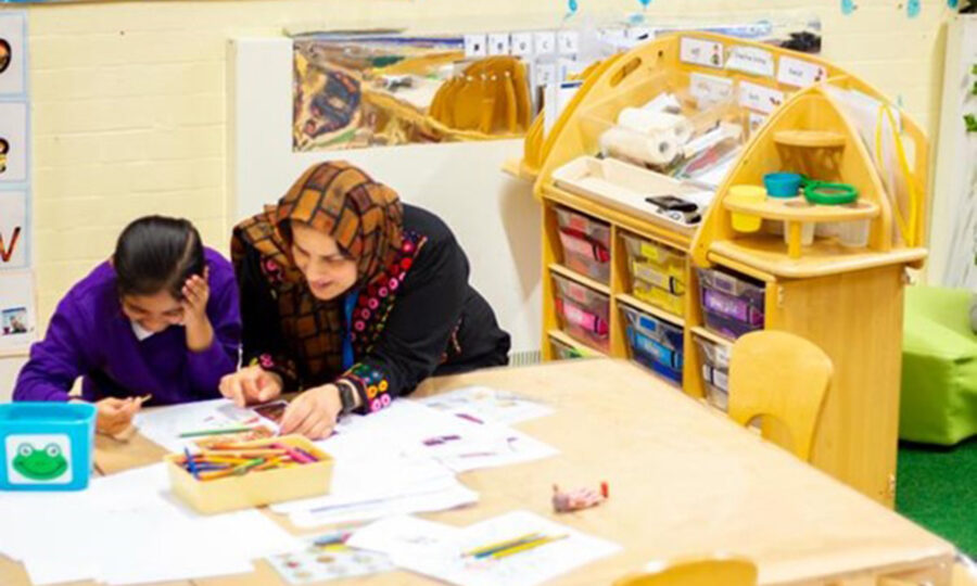 Bibi at the centre helping a young girl at a table with pens and paper on