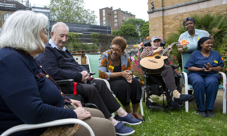 Care home manager Fatma and a staff member laughing with residents in the garden of the care home, by Regent's Canal