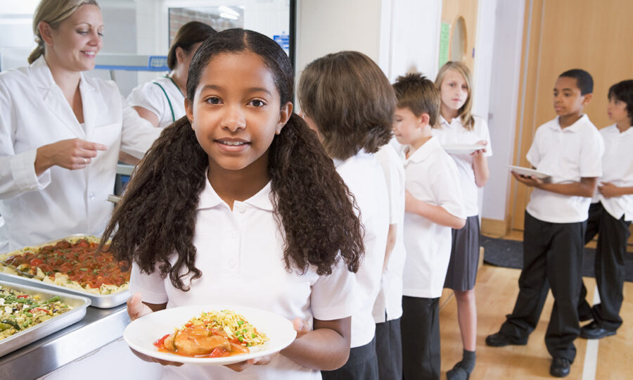 Young girl stood holding plate of food in school canteen
