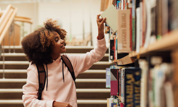 Young Black girl taking a book from a bookshelf