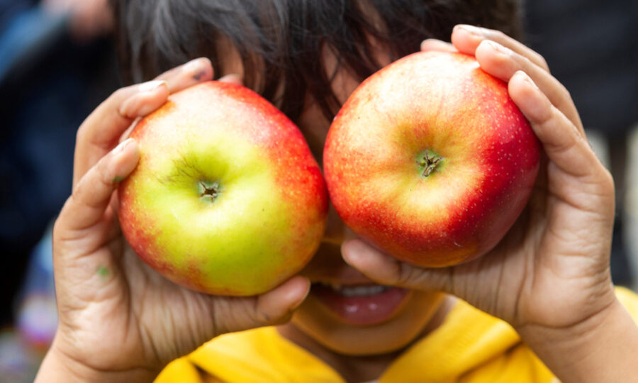 Close up shot of a boy holding an apple over each of his eyes