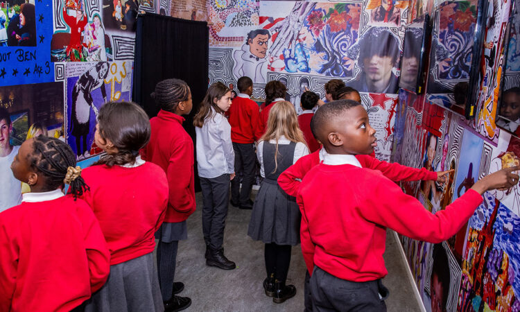 A group of children in school uniform looking at images on a wall at the Ben Kinsella exhibition