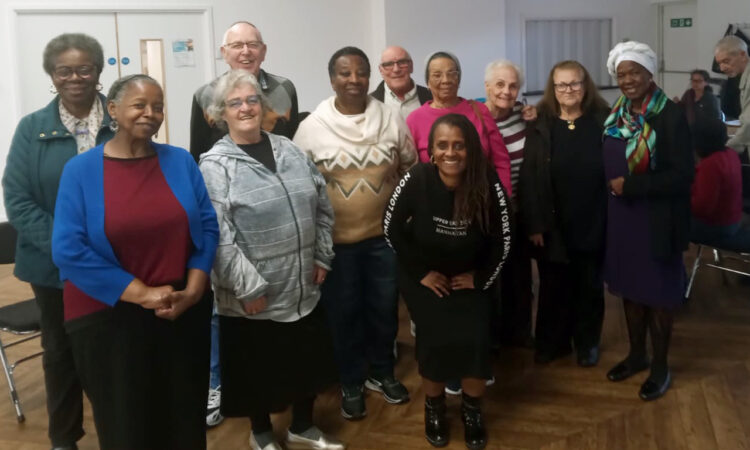 A group of older residents of different ethnicities posing and smiling, with Cyrlene crouched down in the front, in a community centre hall