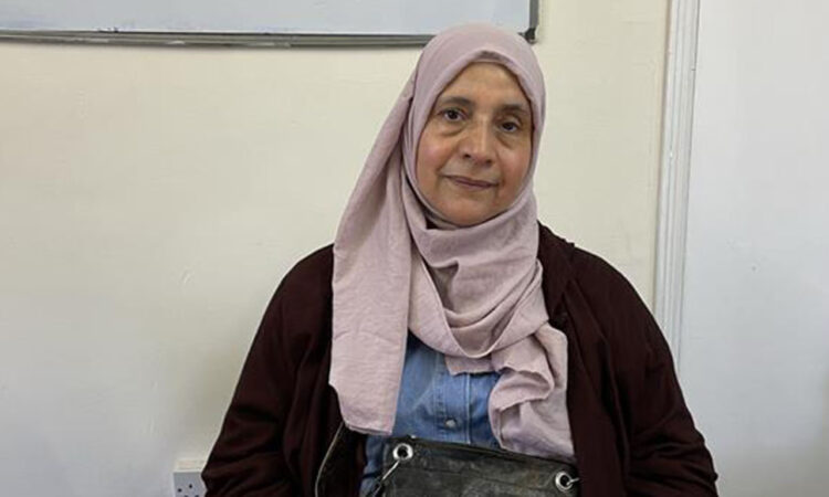 Nahed Mahmoud sat at a desk with a bag on her lap and wearing a pink hijab, looking at camera