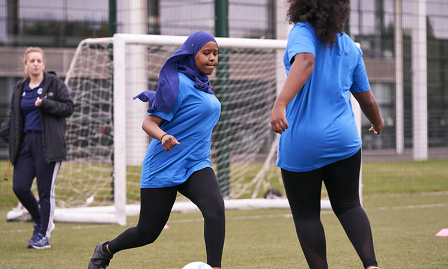 Teen girl in hijab kicking a ball about to be tackled by another teen girl