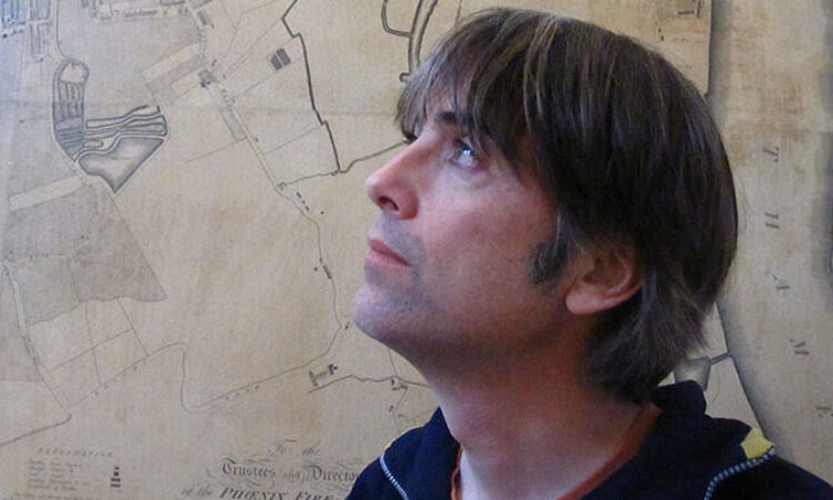 Close up of Peter Carty looking up and to the right with a map in the background