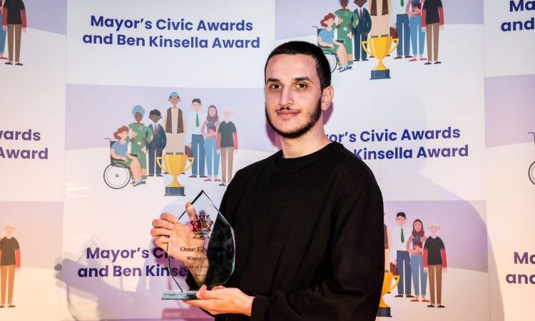 Omar standing on stage at the Awards Evening with his Mayor’s Civic Award.