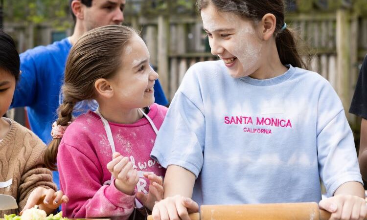 Two girls smiling with flour on their faces cooking