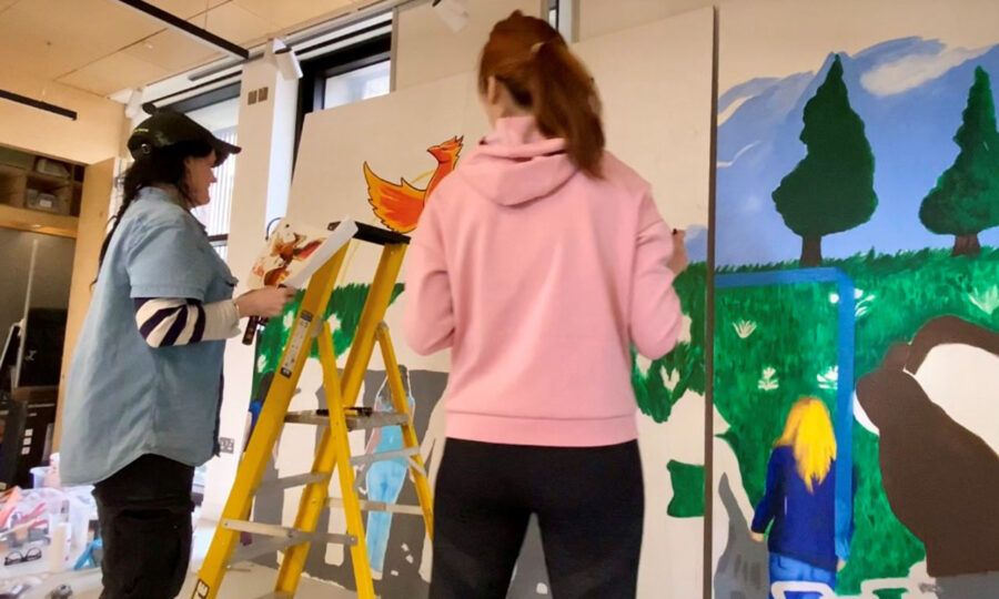 Two women with backs to camera painting on large canvases