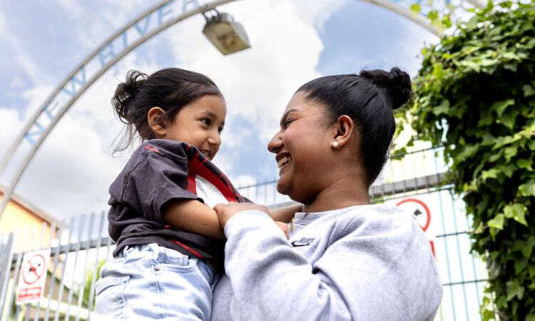 Fathima holding her child, Zain, looking at each other and smiling in front of the New River Green Children's Centre arched entrance