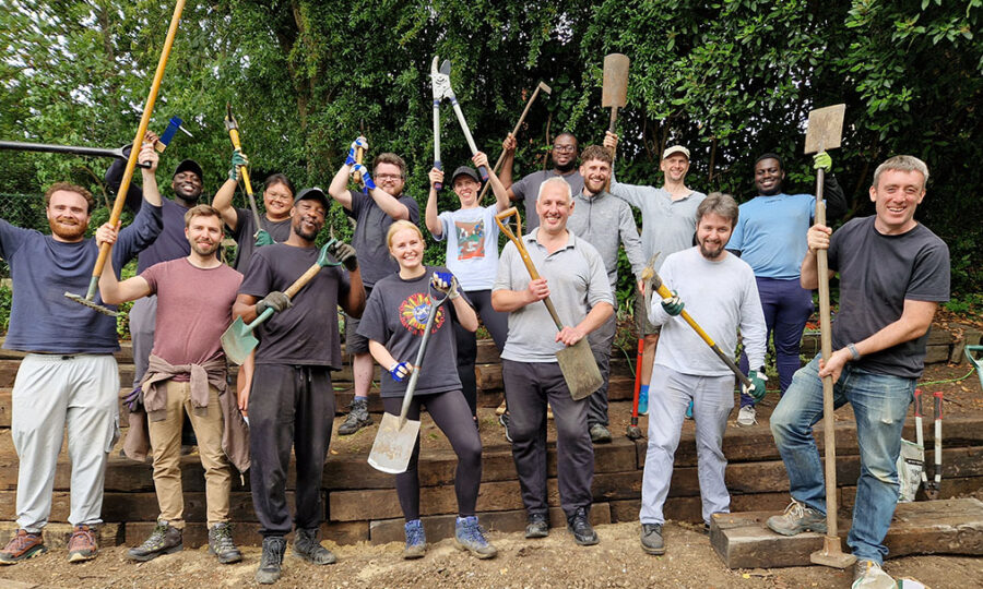 A mixed group of people smiling to camera and holding gardening tools in Olden Community Garden