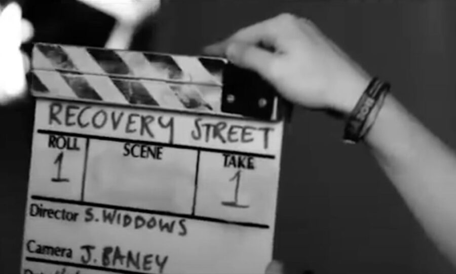 Person holding a film clapperboard that says Recovery Street on it