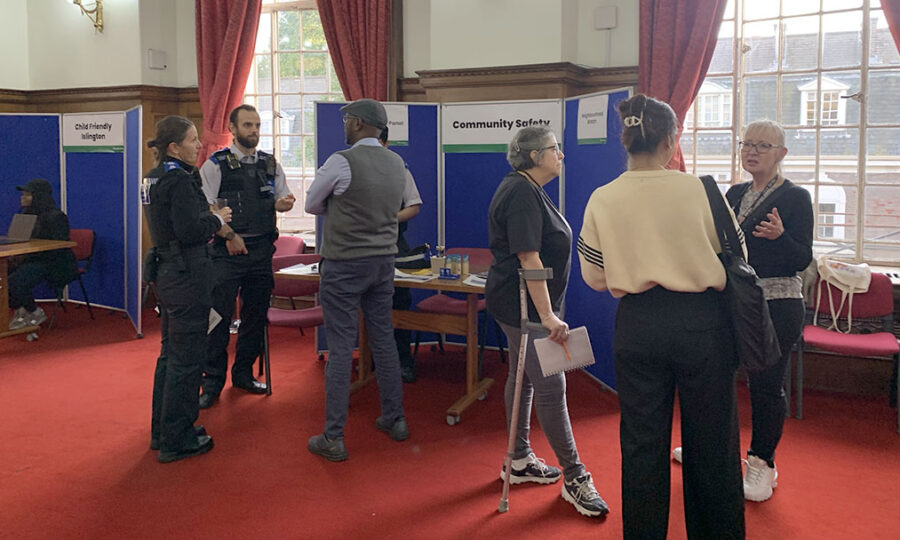 A group of people in a Town Hall committee room in front of a stall that says 'community safety'