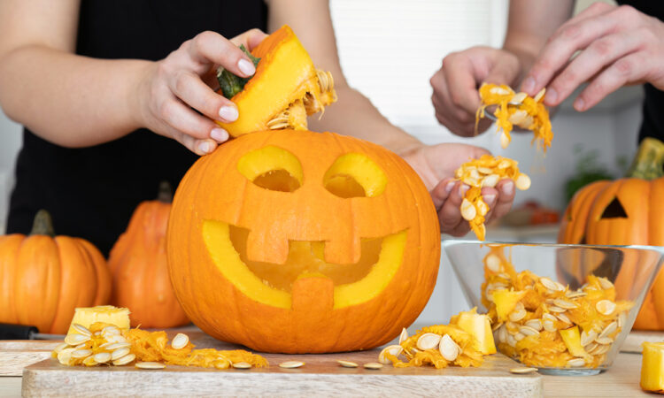 Close up of two people's hands carving a Halloween pumpkin
