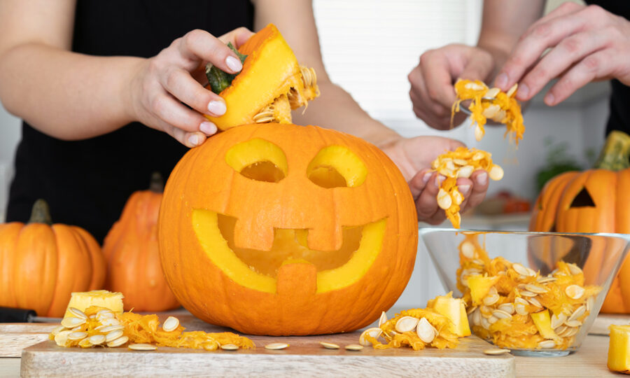 Close up of two people's hands carving a Halloween pumpkin