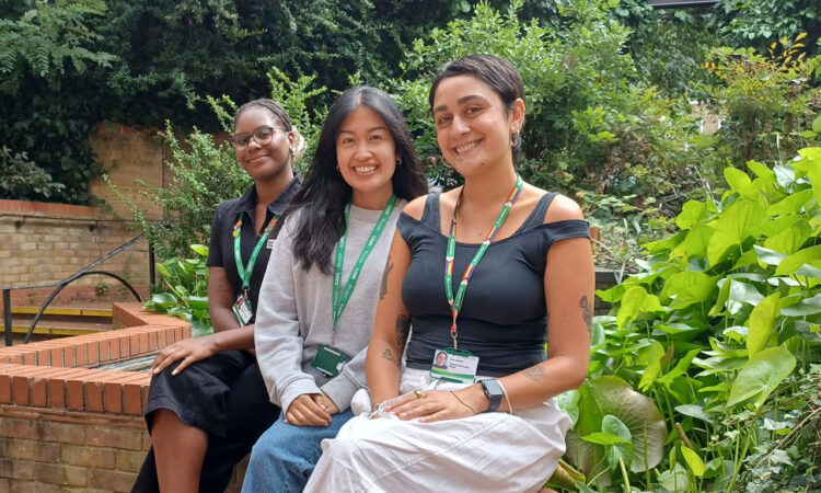 Early help attendance monitors Gretchen Uma and Remy wearing islington lanyards and sat on a wall in a green garden