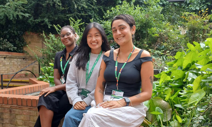 Early help attendance monitors Gretchen Uma and Remy wearing islington lanyards and sat on a wall in a green garden