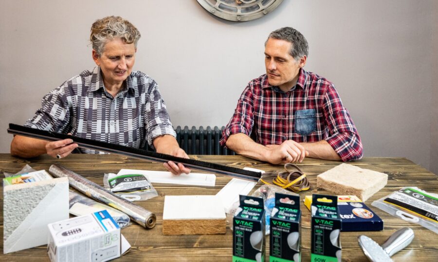 Two people sitting at a table which is holding DIY energy saving items like insulation and LED lightbulbs