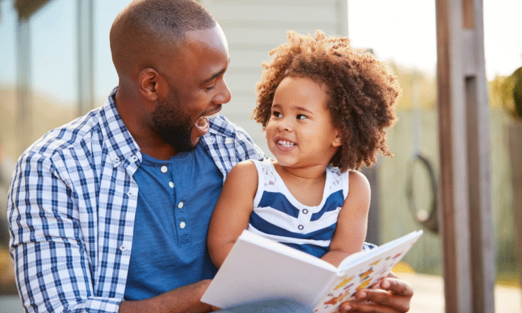A father smiling and reading a book to his daughter