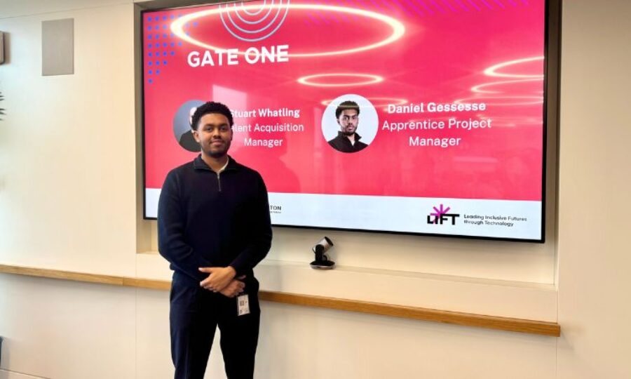 Young man smiling at the camera stood in front of a red board which is introducing him