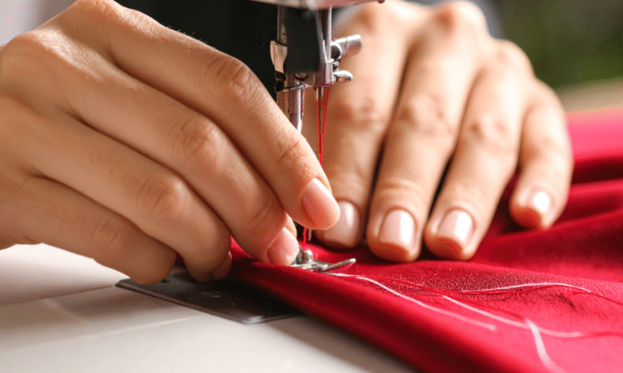 A pair of hands using a sewing machine to sew red fabric