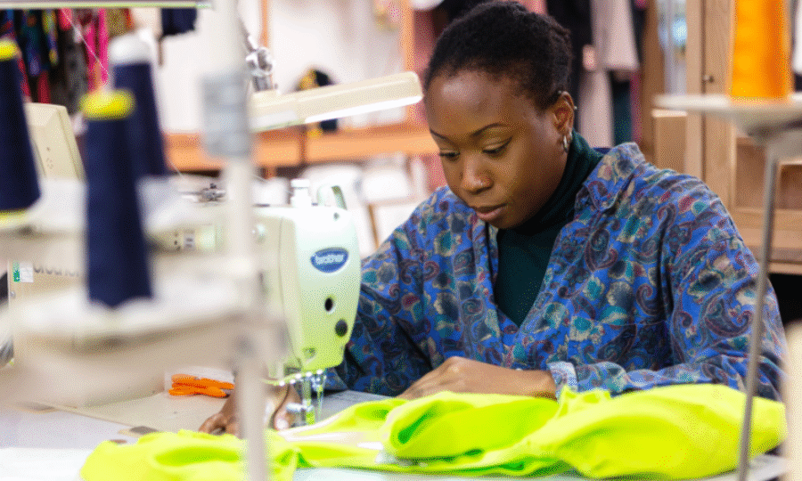 A black woman using a sewing machine to stitch a bright coloured fabric