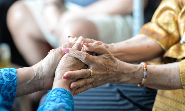 Two hands with visible wrinkles and signs of age on top of each other in a warm embrace