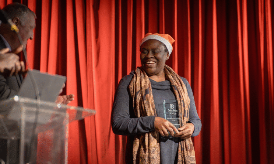 Woman on stage in front of a red curtain smiling and holding an award