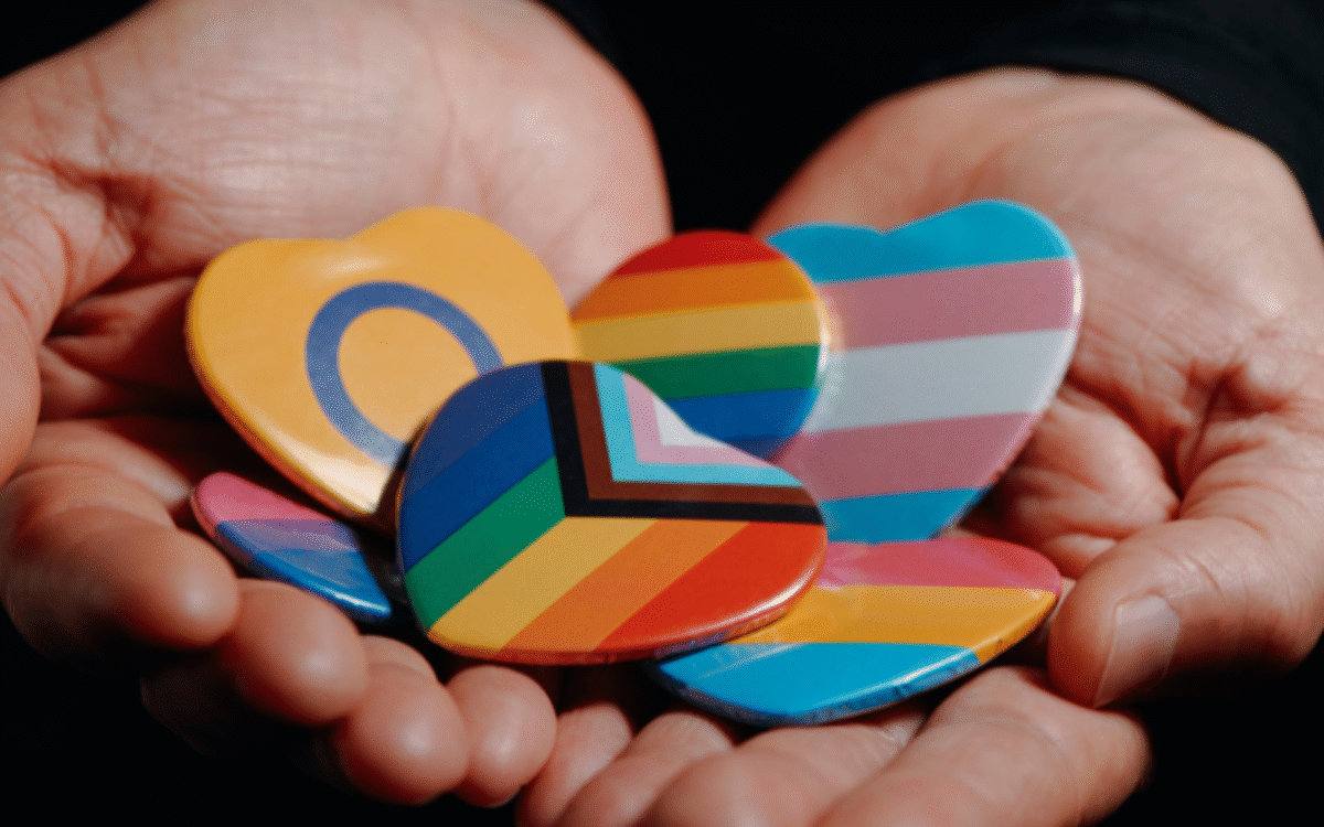 Person holding different LGBTQ+ pins in their open palms