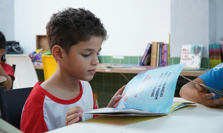 A young child wearing a white and red jersey reading a book