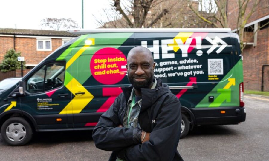 Man looking at camera smiling with colourful youth van in the background
